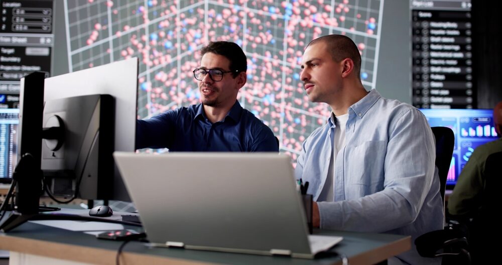 Collaborateurs analysant des données sur écrans informatiques dans un environnement technologique, illustrant les métiers IT, l’infrastructure et le développement des systèmes d’information - Recrutement OCEA Smart Building